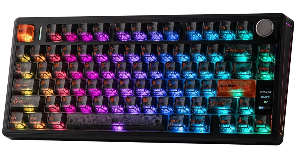 Klawiatura mechaniczna z podświetleniem RGB, posiadająca czarne klawisze z przezroczystymi nakładkami. Na klawiaturze widoczny jest wyświetlacz z godziną 17:57:06.
