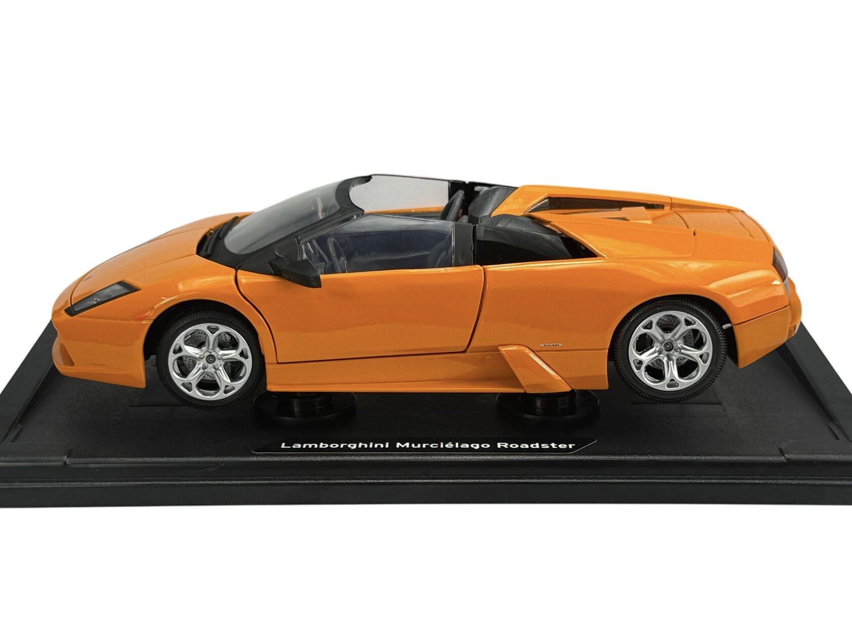 Pomarańczowy model samochodu sportowego na czarnej podstawce z napisem \'Lamborghini Murciélago Roadster\'. Samochód ma otwarty dach i srebrne felgi.