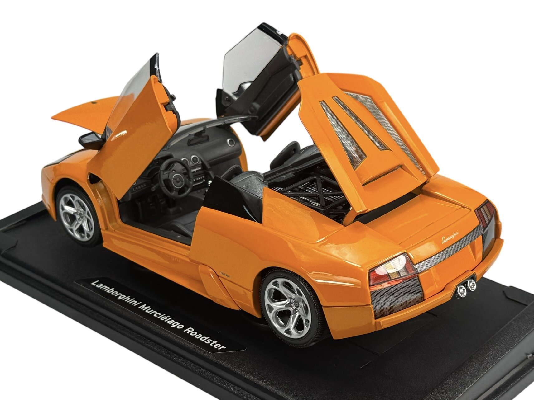 Pomarańczowy model samochodu sportowego z otwartymi drzwiami i klapą silnika, umieszczony na czarnej podstawce z napisem \'Lamborghini Murcielago Roadster\'.