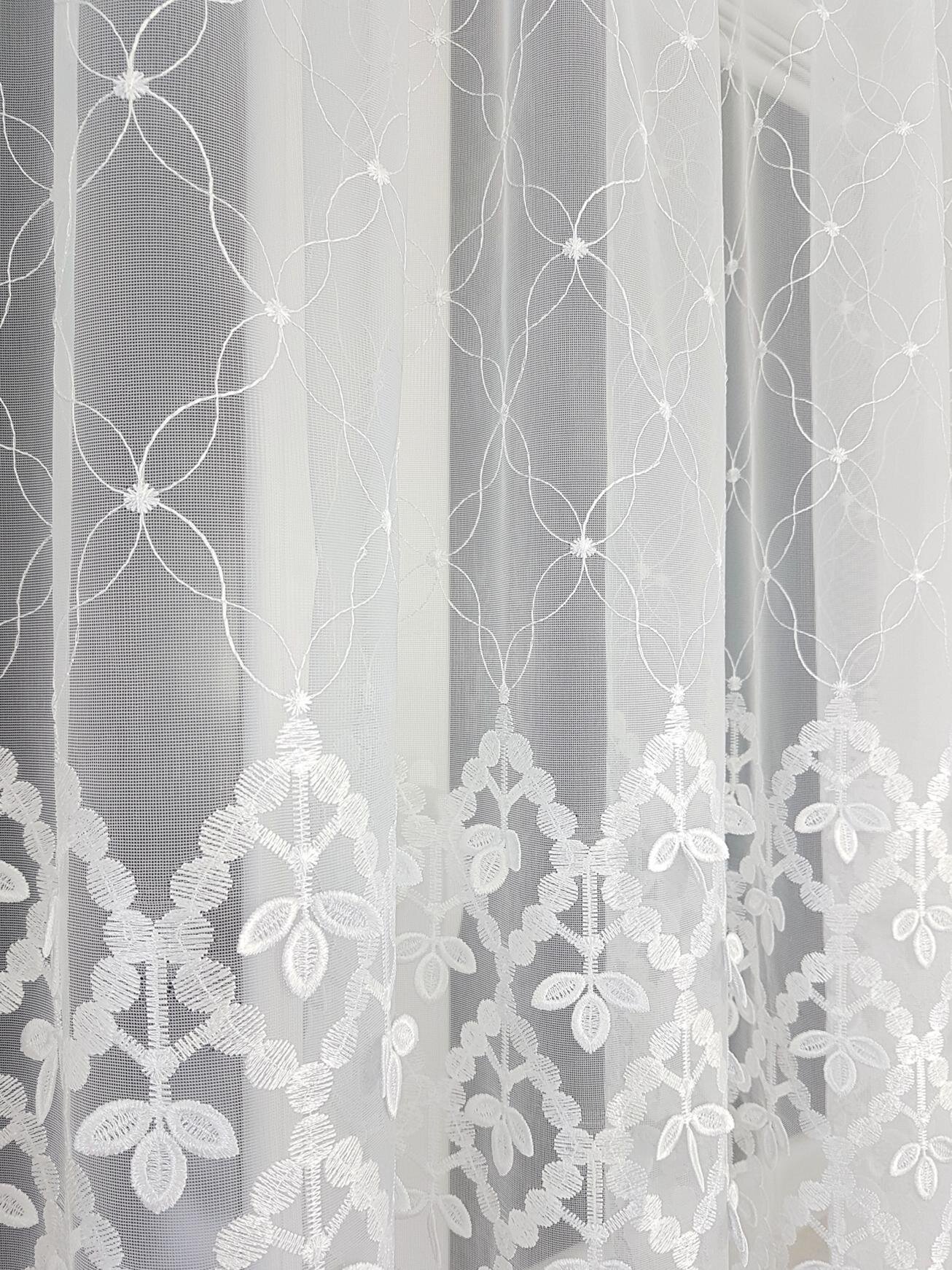 Biała firana z markizety z delikatnym, geometrycznym wzorem 3D, przedstawiającym kwiatowe motywy i linie tworzące okręgi. Tkanina jest półprzezroczysta, co pozwala na przenikanie światła.