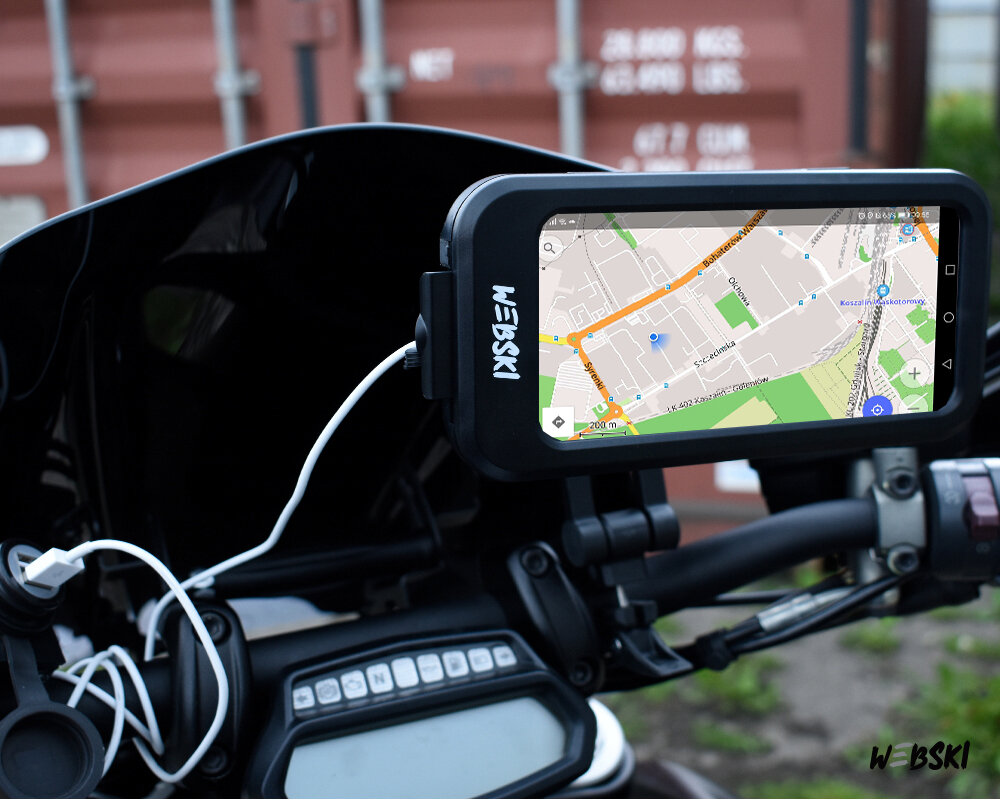 Na zdjęciu widać uchwyt rowerowy lub motocyklowy z zamocowanym telefonem, na którym wyświetlana jest mapa. Na uchwycie widoczne jest logo \'W-EBSKI\'.