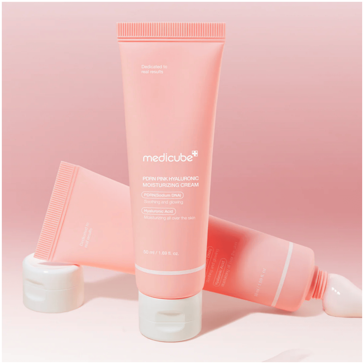 Na obrazie widoczne są dwa różowe opakowania kremu do twarzy z napisem \'medicube PDRN Pink Hyaluronic Moisturizing Cream\'. Opakowania mają białe zakrętki i znajdują się na różowym tle.
