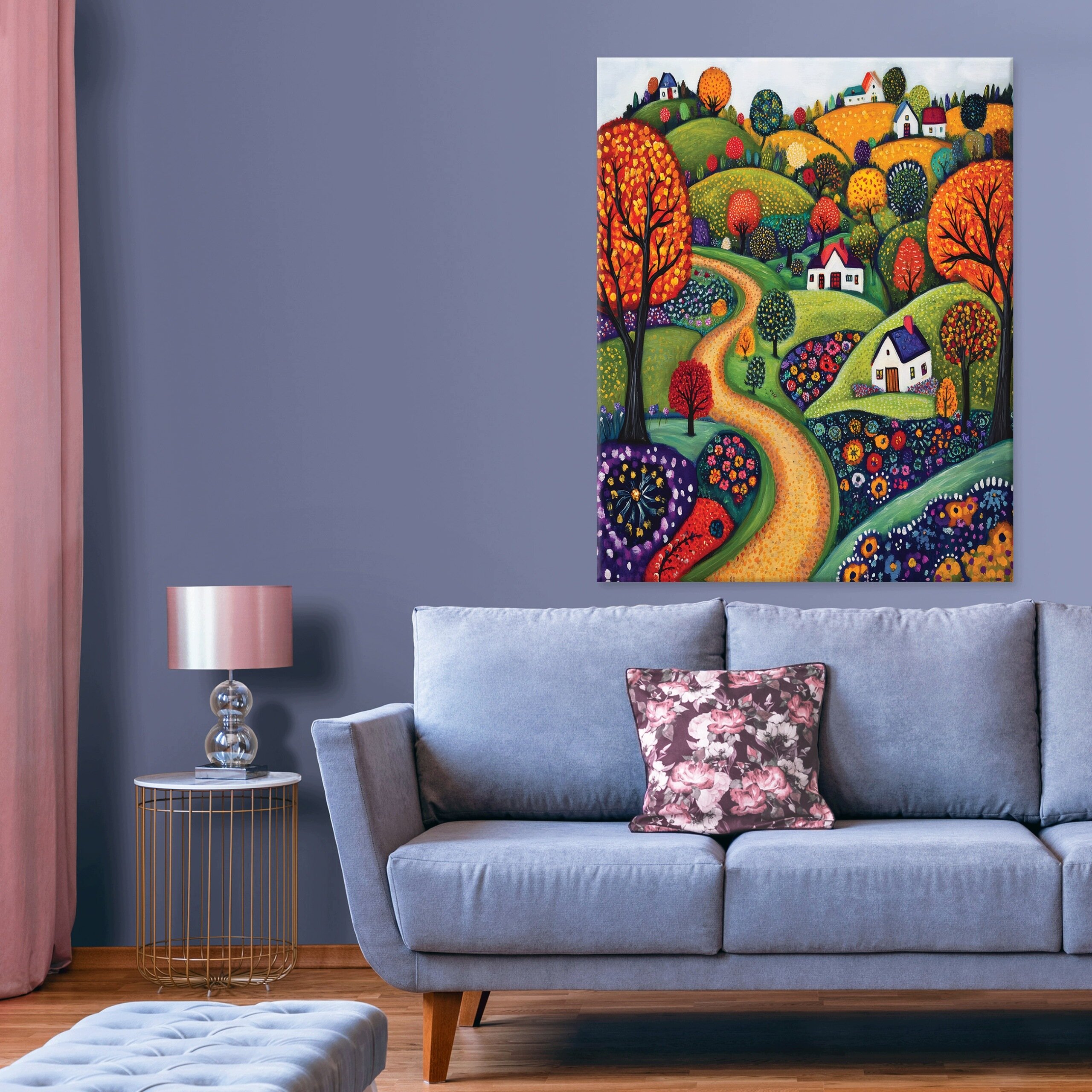 Na ścianie wisi kolorowy obraz przedstawiający pejzaż z pomarańczową drogą, drzewami i domkami. W pokoju znajduje się szara sofa z kwiecistą poduszką oraz stolik z lampą.