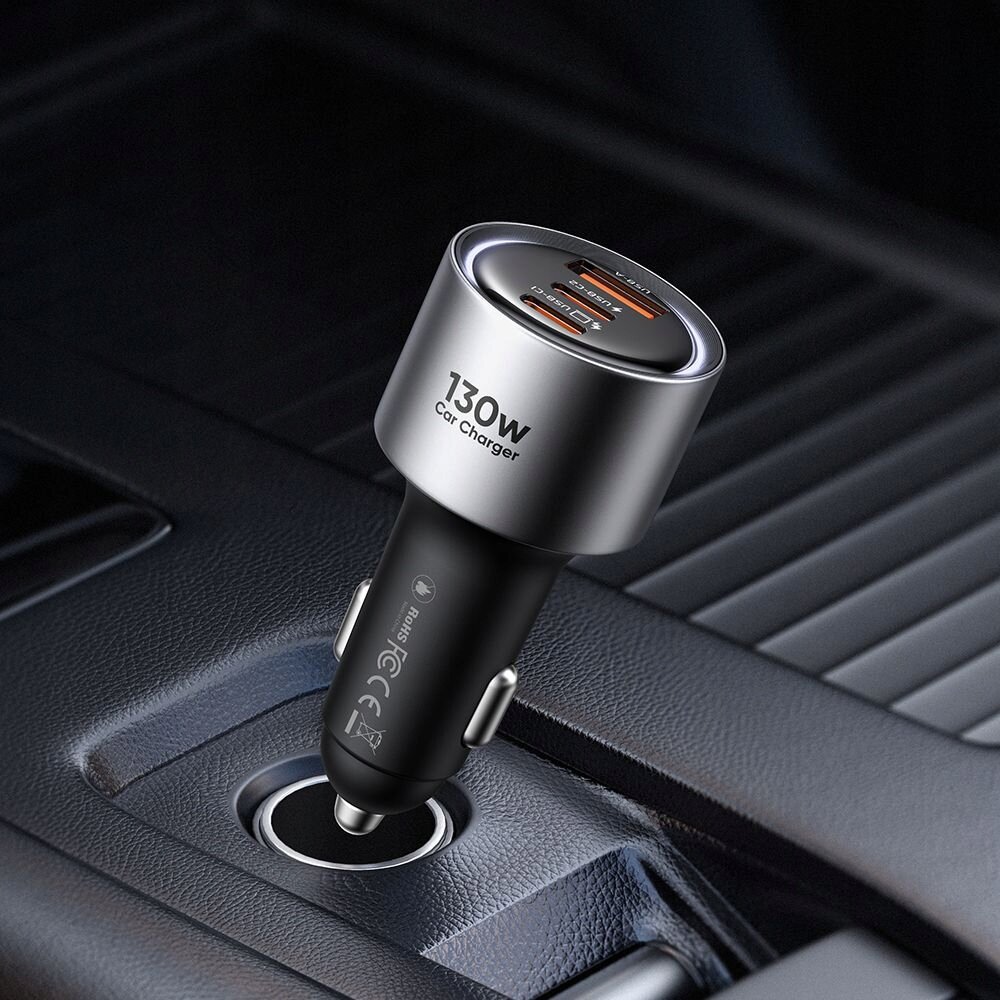 Srebrno-czarna ładowarka samochodowa z trzema portami (2x USB-C, 1x USB-A) umieszczona w gnieździe zapalniczki. Na ładowarce widoczny jest napis \'130W Car Charger\'.