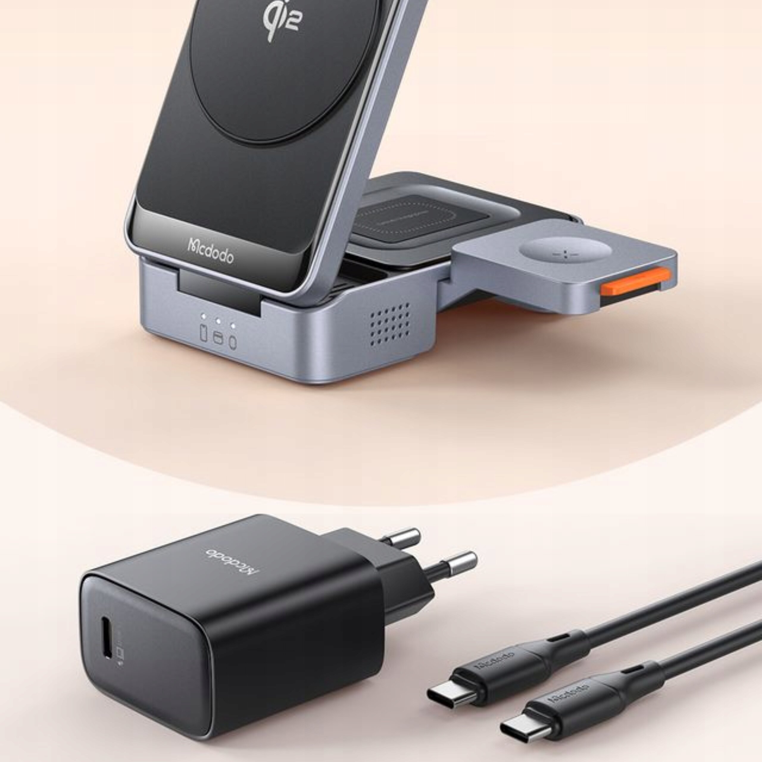 Na obrazie widoczna jest stacja dokująca z logo \'Mcdodo\' oraz oznaczeniem \'Qi2\', a także czarny adapter z dwoma kablami USB-C. Stacja ma metaliczny wygląd z pomarańczowym elementem, a adapter jest czarny z logo \'Mcdodo\'.