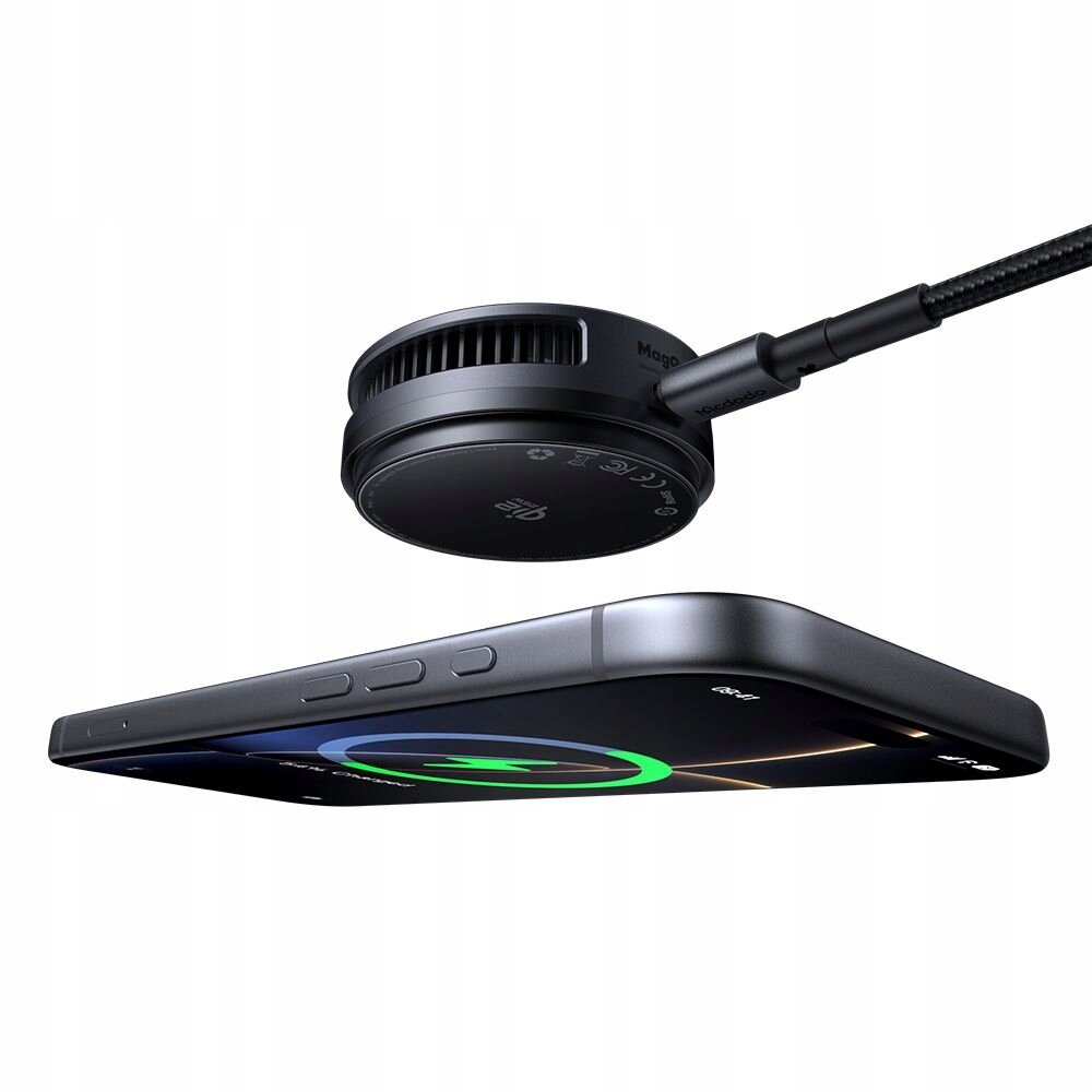 Na obrazie widoczna jest czarna ładowarka indukcyjna z napisem \'Magsafe\' oraz smartfon z wyświetlonym symbolem ładowania. Ładowarka jest podłączona kablem, a na jej powierzchni znajdują się oznaczenia techniczne.