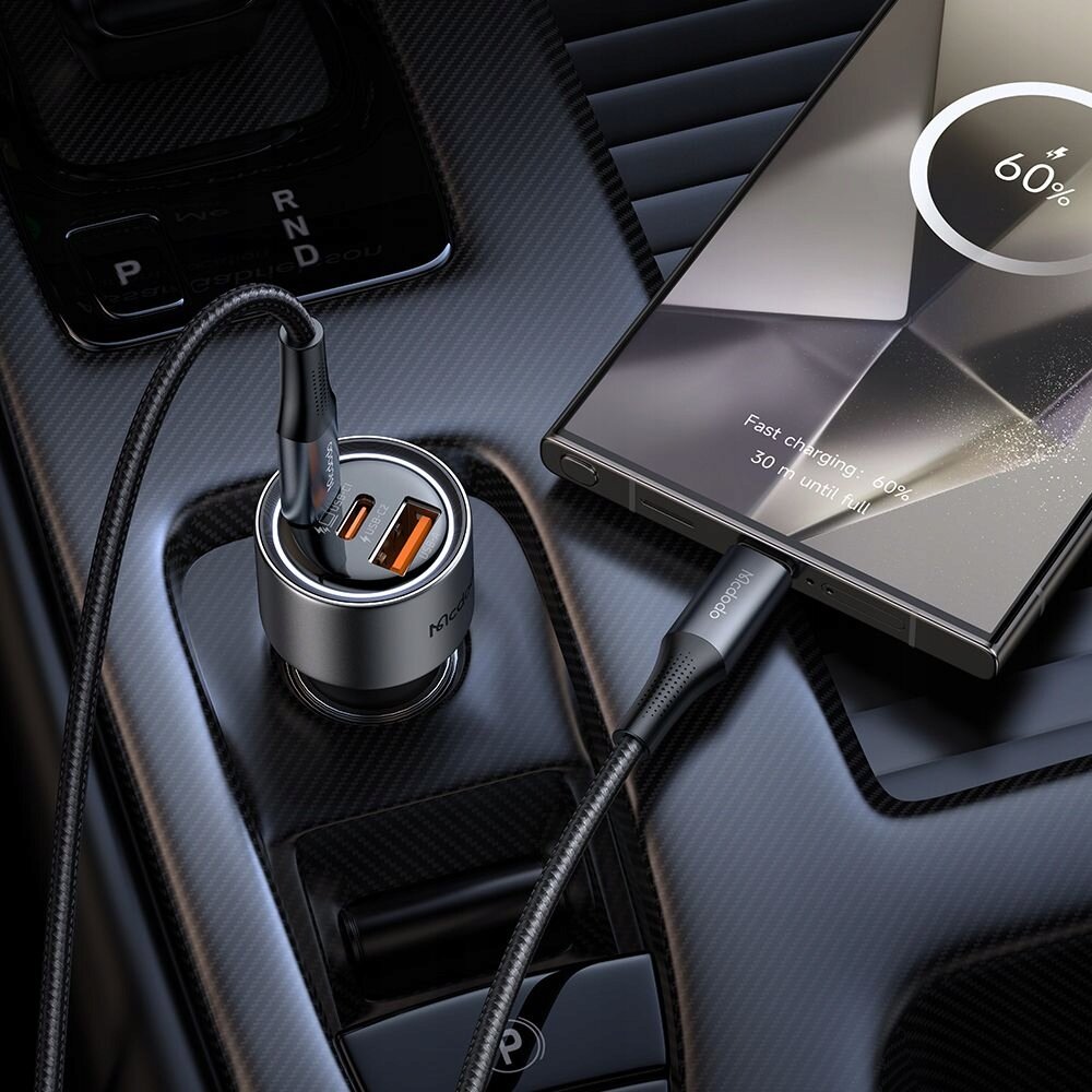 Na zdjęciu widać srebrną ładowarkę samochodową z dwoma portami USB-C i jednym USB-A, podłączoną do telefonu. Na ekranie telefonu widoczny jest napis: \'Fast charging - 60%, 30 min until full\'.