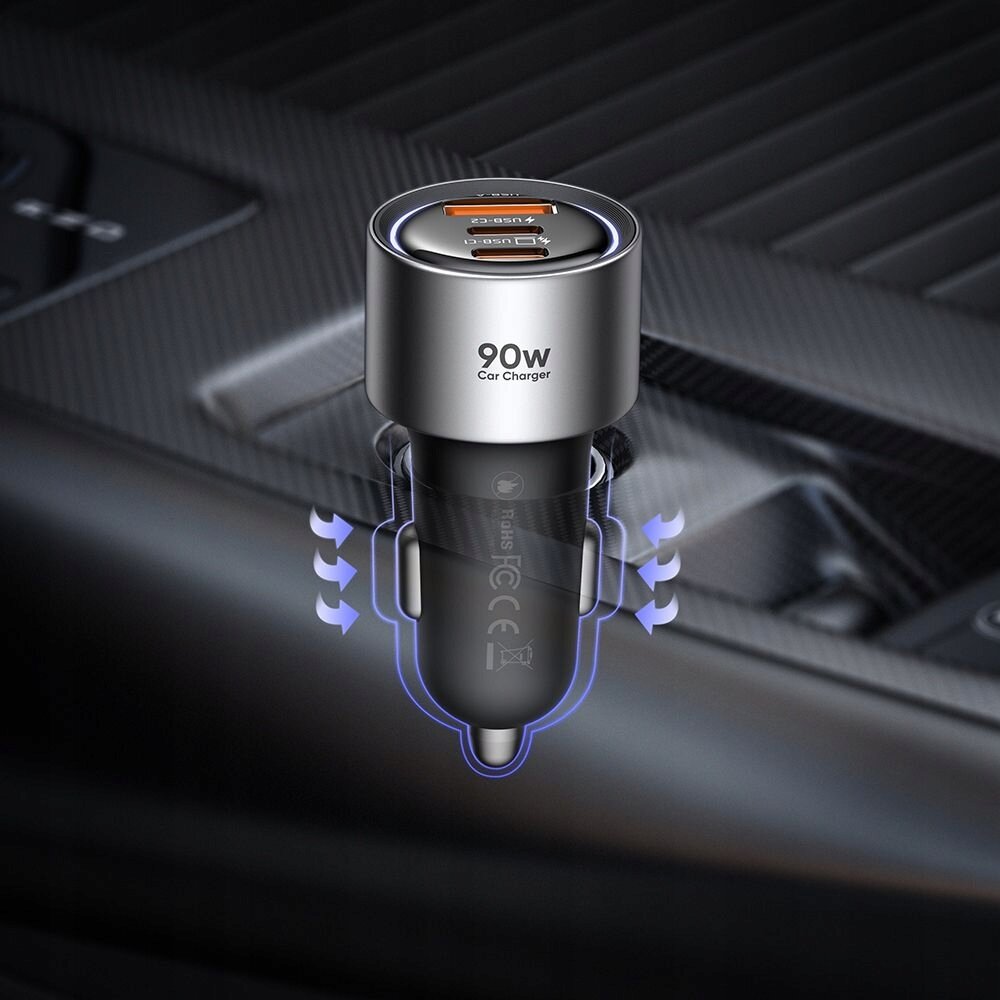 Na obrazie widoczna jest szybka ładowarka samochodowa z trzema portami: dwoma USB-C i jednym USB-A, z oznaczeniem \'90W Car Charger\'. Ładowarka jest umieszczona w gnieździe samochodowym, a wokół niej widoczne są niebieskie strzałki wskazujące przepływ powietrza.