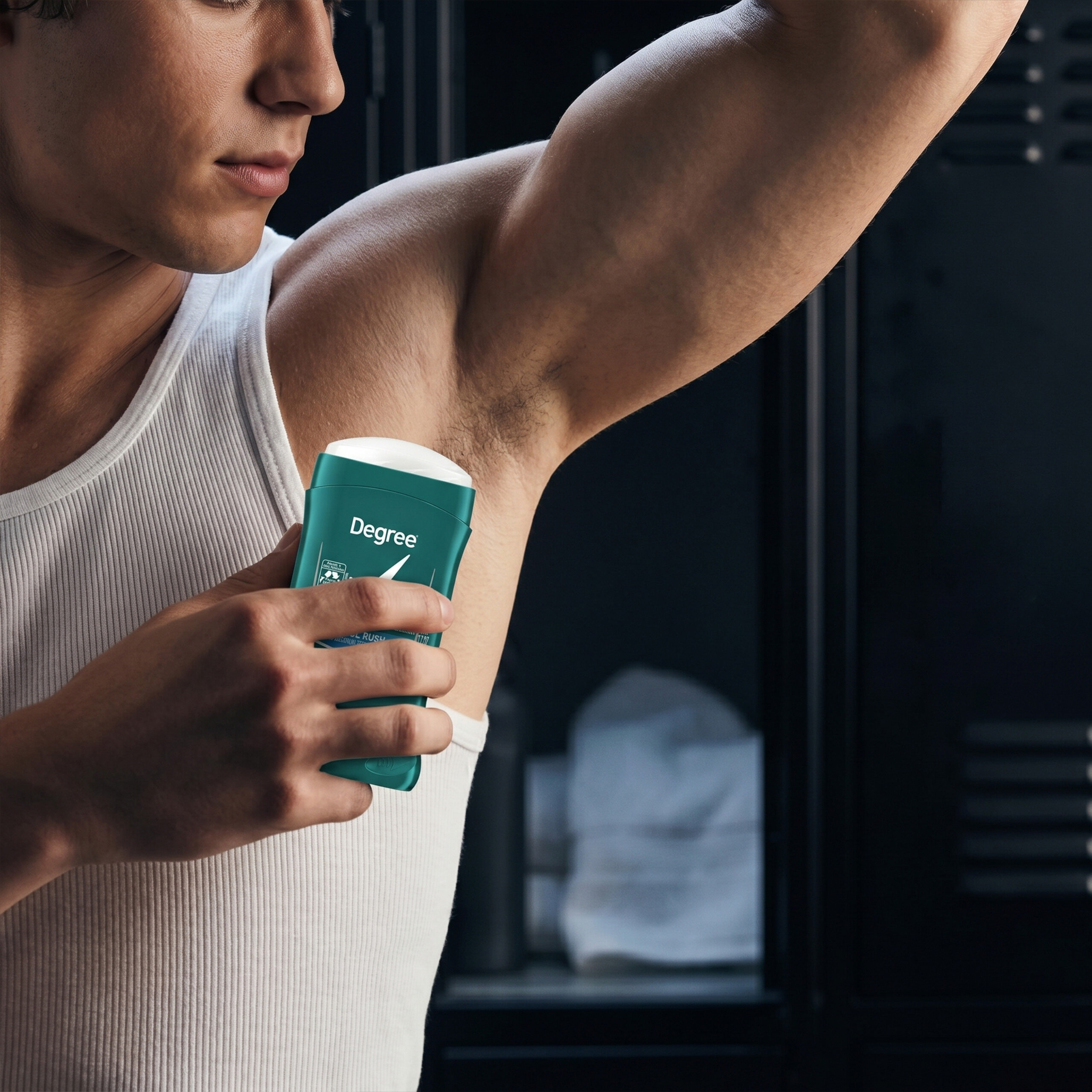 Osoba w białej koszulce aplikuje antyperspirant w sztyfcie pod pachę. Na opakowaniu widoczny jest napis \'Degree\'.