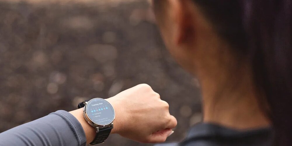 Osoba patrzy na smartwatch na swoim nadgarstku. Wyświetlacz zegarka pokazuje kilka ikon i tekst, ale szczegóły nie są czytelne.