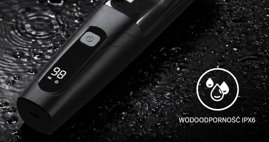 Czarna strzyżarka z wyświetlaczem pokazującym liczbę 98 i symbolem baterii, leży na mokrej powierzchni. Obok znajduje się symbol kropli wody z napisem \'WODOODPORNOŚĆ IPX6\'.