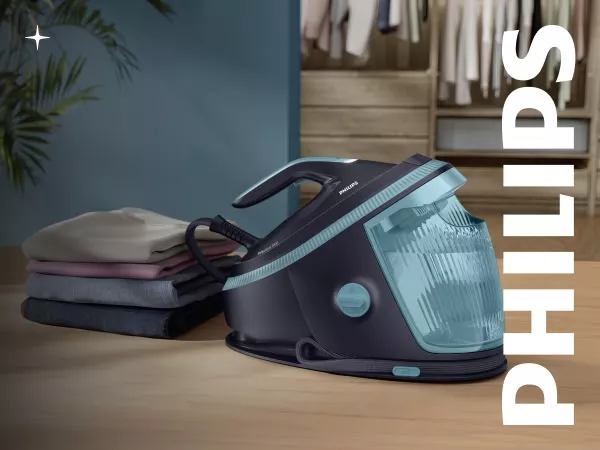Generator pary w ciemnym kolorze z przezroczystym, niebieskim zbiornikiem na wodę, obok stosu złożonych ubrań. Na obrazie widoczne jest logo \'PHILIPS\'.