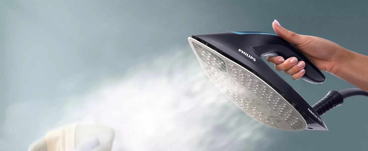 Osoba trzyma żelazko parowe z widocznym logo PHILIPS, z którego wydobywa się para. Na uchwycie widoczny jest napis \'PerfectCare 7000\'.
