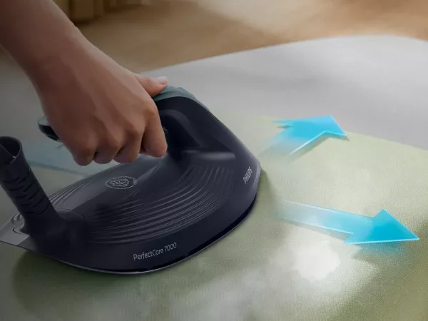 Osoba prasuje tkaninę za pomocą generatora pary z napisem \'PerfectCare 7000\' i logo \'PHILIPS\'. Widoczne są niebieskie strzałki wskazujące kierunek ruchu.