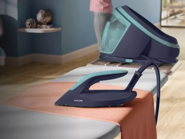 Na desce do prasowania znajduje się żelazko parowe z napisem \'PHILIPS\', a w tle widoczny jest generator pary w kolorze granatowym z turkusowymi akcentami.