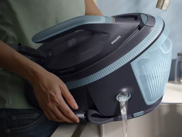 Osoba trzyma generator pary, z którego wylewa się woda. Na urządzeniu widoczne jest logo \'PHILIPS\'.