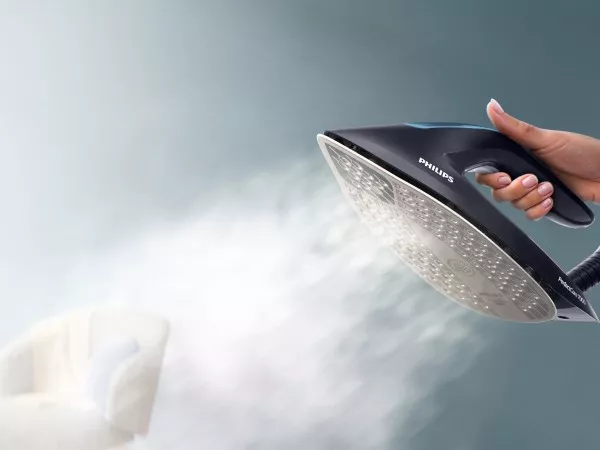 Osoba trzyma żelazko, z którego wydobywa się intensywna para. Na żelazku widoczne jest logo \'PHILIPS\'.