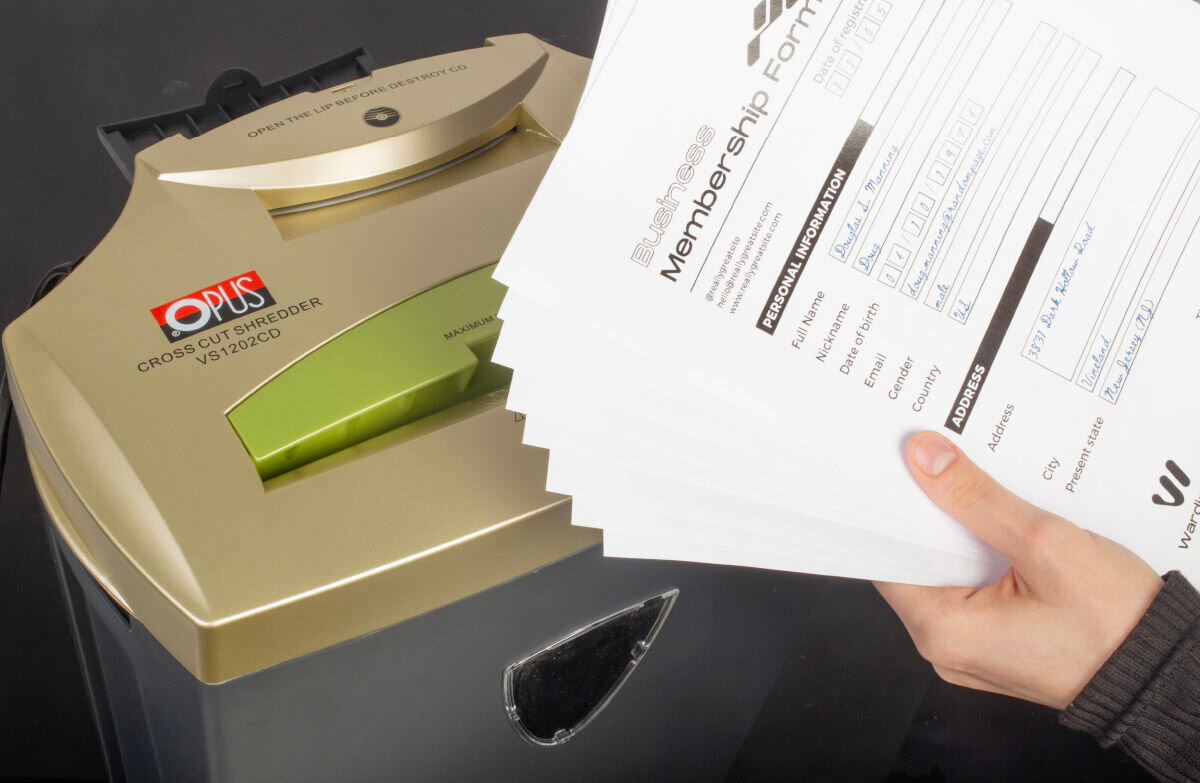 Na obrazie widoczna jest niszczarka z logo \'OPUS\' i napisem \'CROSS CUT SHREDDER VS1202CD\'. Obok urządzenia osoba trzyma stos dokumentów z widocznym tekstem \'Business Membership Form\'.