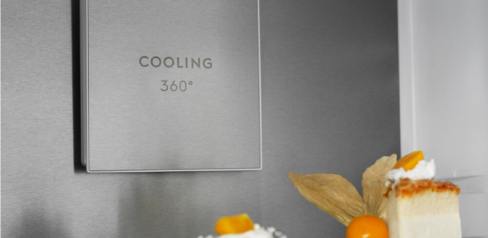 Na obrazie widoczny jest fragment wnętrza lodówki z napisem \'COOLING 360°\' na metalowej powierzchni. Na półce znajdują się kawałki ciasta z owocami.