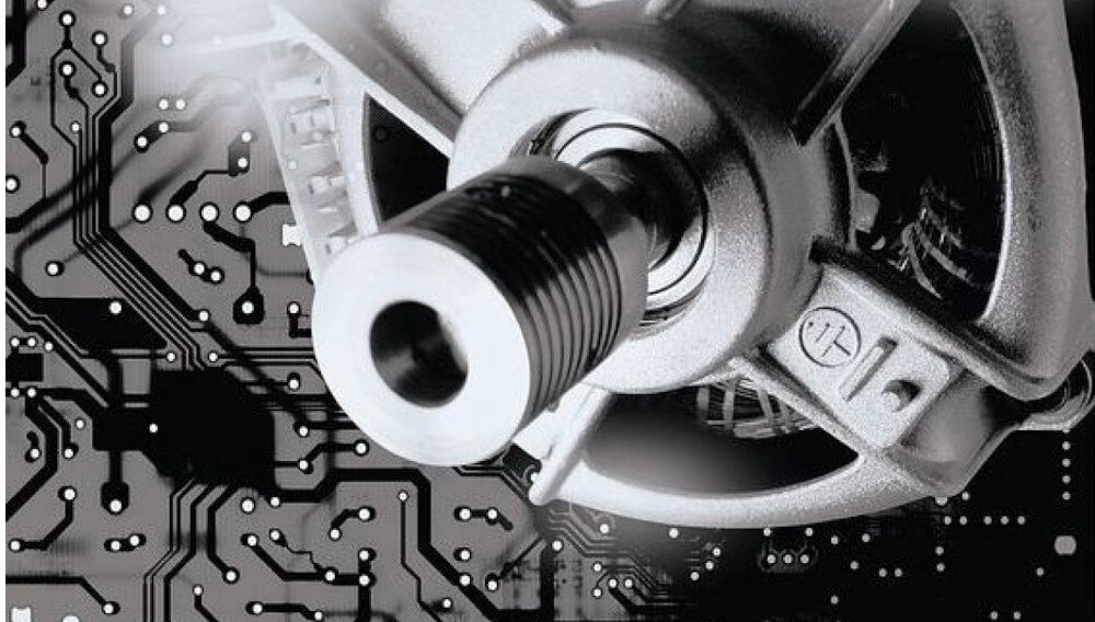 Obraz przedstawia metalowy element mechaniczny na tle płytki drukowanej z widocznymi ścieżkami i punktami lutowniczymi.
