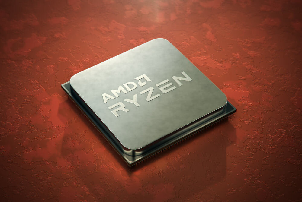 Na obrazie widoczny jest procesor z napisem \'AMD RYZEN\' na metalicznej powierzchni, umieszczony na czerwonym tle.