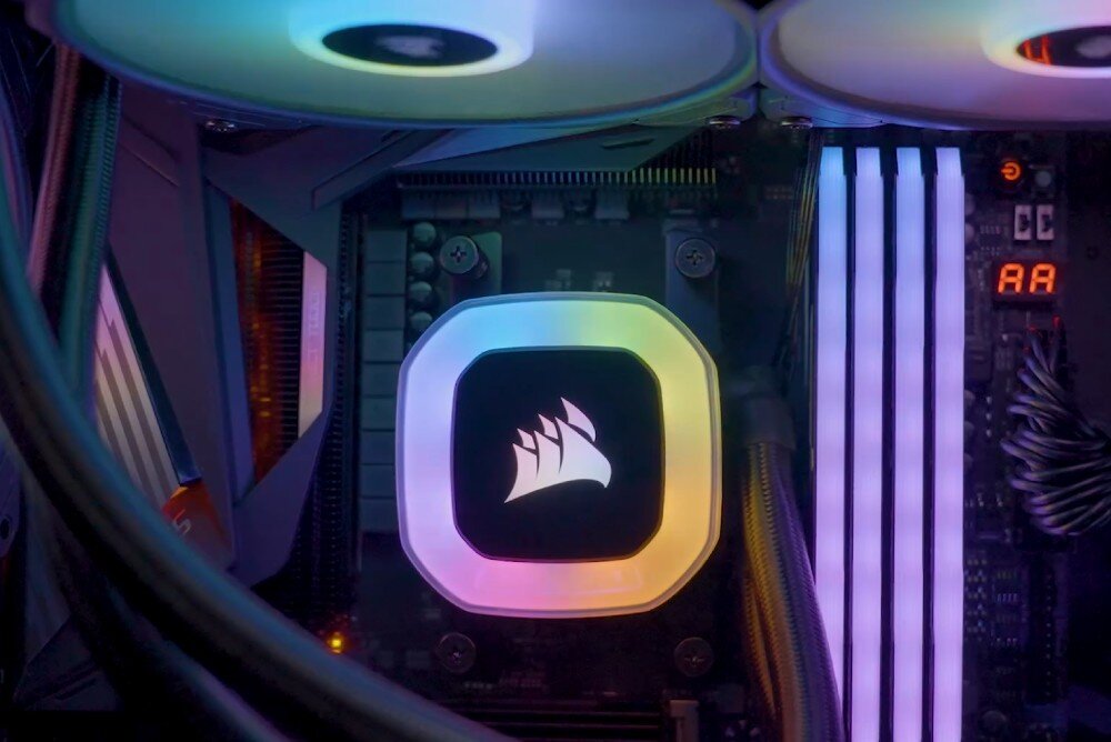 Obraz przedstawia wnętrze komputera z podświetlanym logo Corsair na chłodzeniu procesora. Obok widoczne są podświetlane moduły pamięci RAM oraz wyświetlacz diagnostyczny z cyframi \'AA\'.