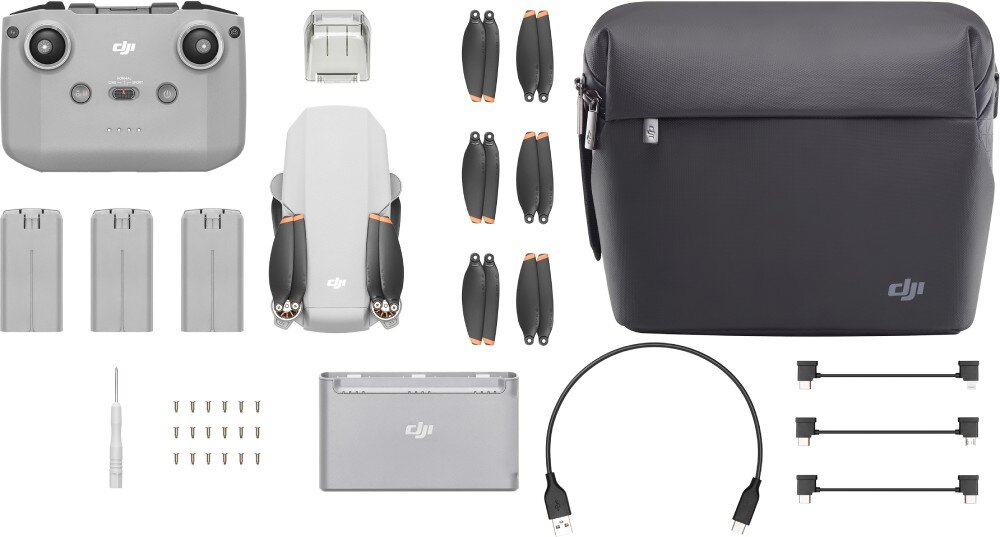Na obrazie znajduje się zestaw akcesoriów do drona, w tym kontroler, trzy baterie, śmigła, torba z logo DJI, kabel USB oraz śrubokręt z zapasowymi śrubkami. Wszystkie elementy są ułożone na białym tle.