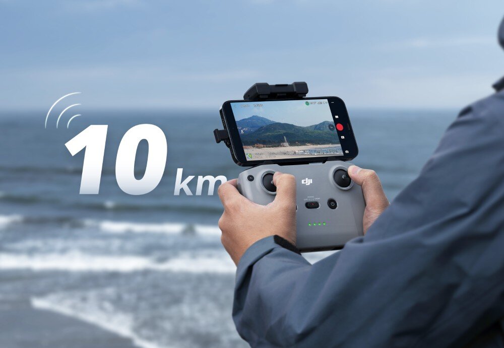 Osoba trzyma kontroler drona z zamocowanym smartfonem, na którym wyświetlany jest obraz z kamery. Na obrazie widoczny jest napis \'10 km\' oraz logo \'dji\'.