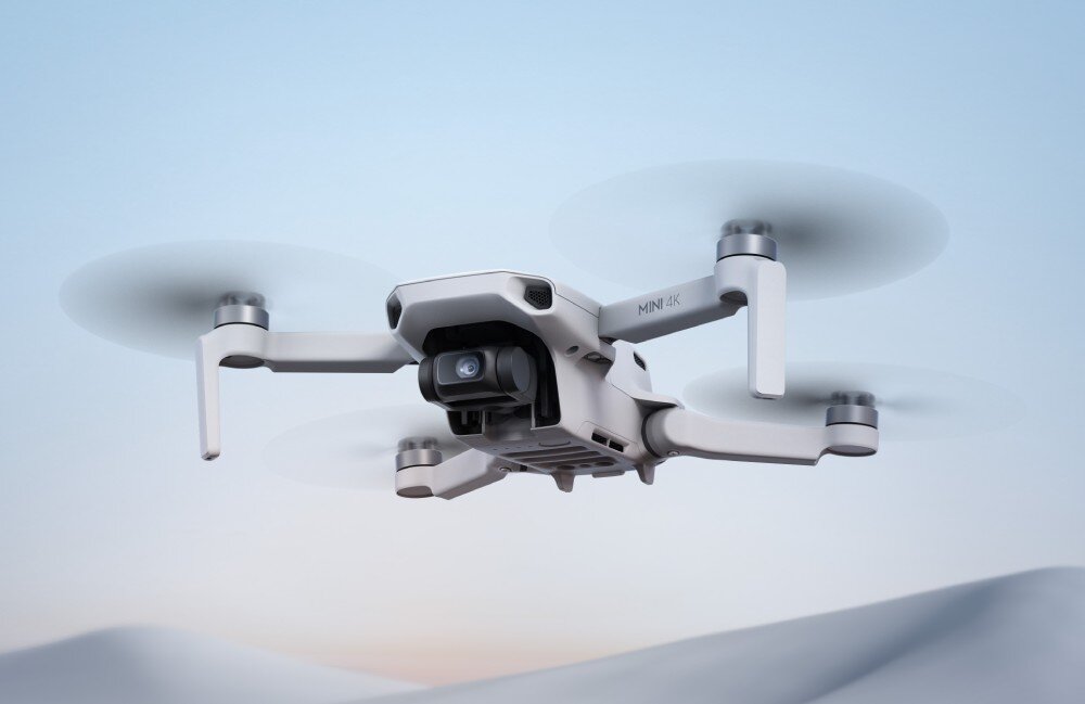 Na obrazie widoczny jest dron w locie, z napisem \'MINI 4K\' na jednym z ramion. Tło jest rozmyte, w odcieniach niebieskiego i białego.