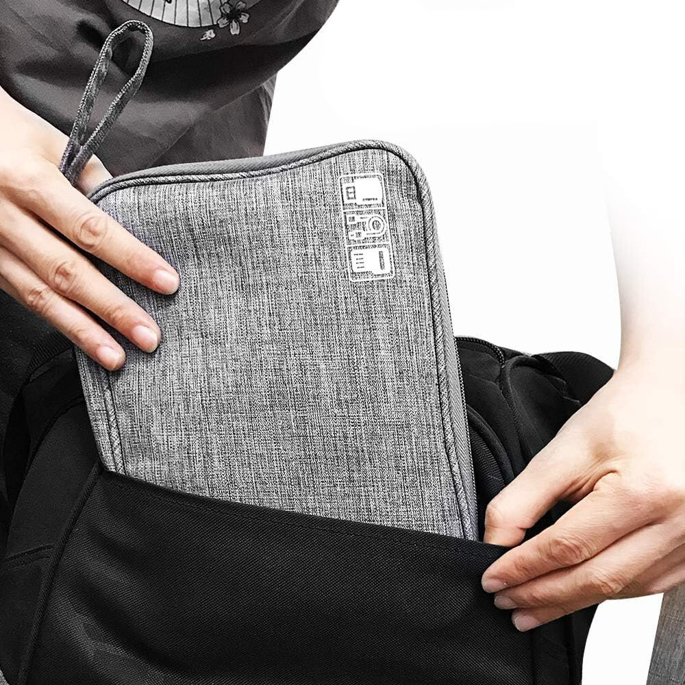Osoba wkłada szare etui organizer na kable do czarnej torby. Na etui widoczne są białe ikony i napisy.