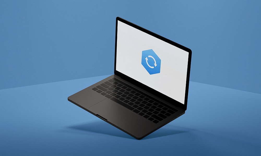 Na obrazie widoczny jest otwarty laptop z wyświetlaczem, na którym znajduje się niebieski sześciokąt z białym symbolem odświeżania. Tło jest jednolite, w kolorze niebieskim.