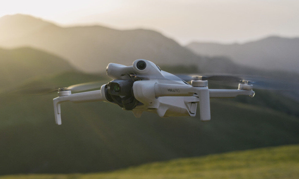 Dron w locie nad zielonymi wzgórzami, w tle widoczne są góry i zachodzące słońce.