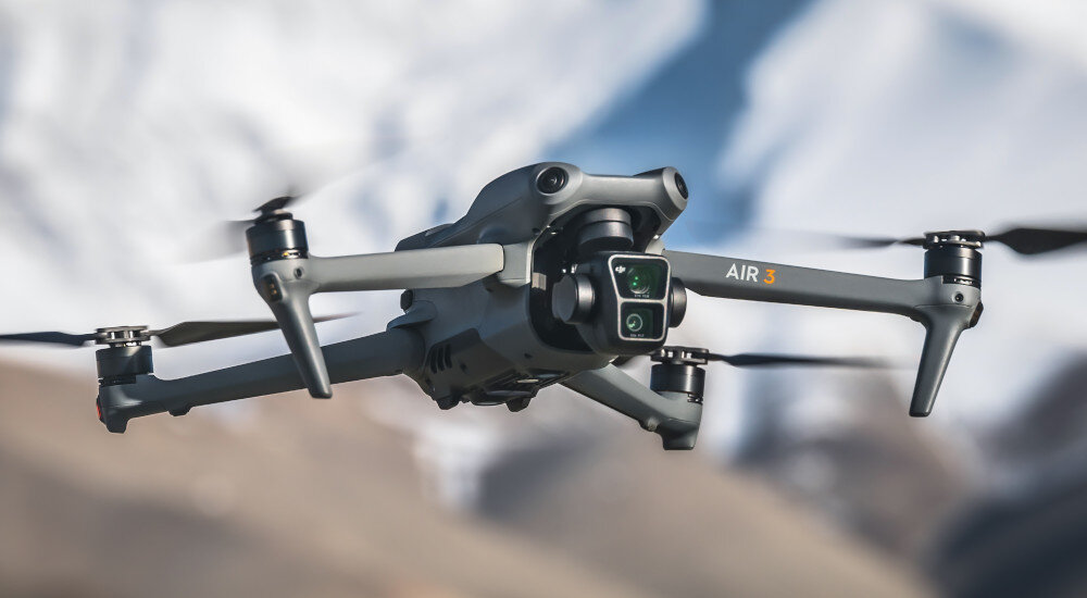 Dron z napisem \'AIR 3\' w locie na tle górskiego krajobrazu.