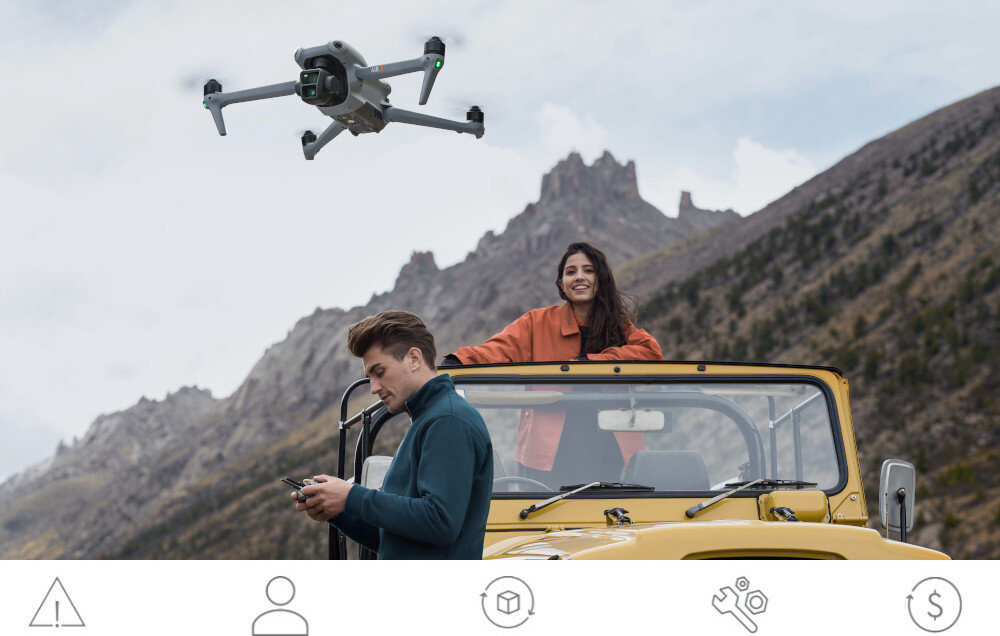 Dron unosi się w powietrzu na tle górskiego krajobrazu, a w żółtym samochodzie terenowym siedzi kobieta i mężczyzna trzymający kontroler. Na dole obrazu widoczne są ikony: ostrzeżenie, osoba, pudełko, narzędzia i symbol dolara.