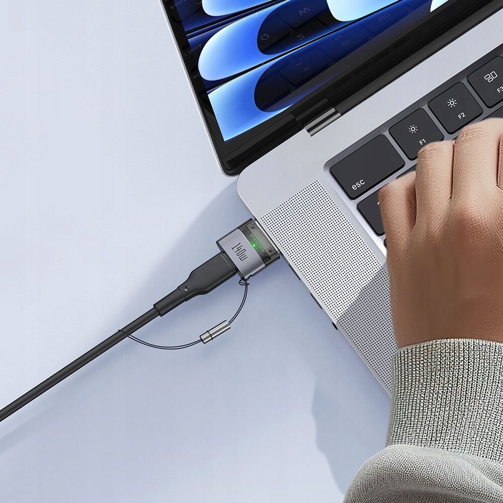 Osoba używa laptopa, do którego podłączony jest adapter magnetyczny z napisem \'140W\'.