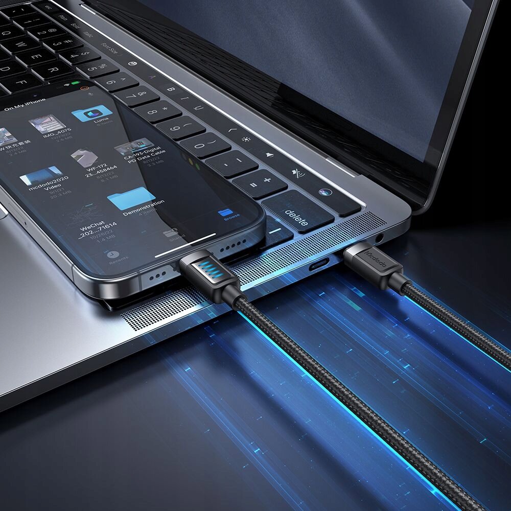 Na obrazie widać laptopa z podłączonym smartfonem za pomocą kabla USB-C Lightning. Kabel ma podświetlenie LED i widoczne jest logo \'mcdodo\'.
