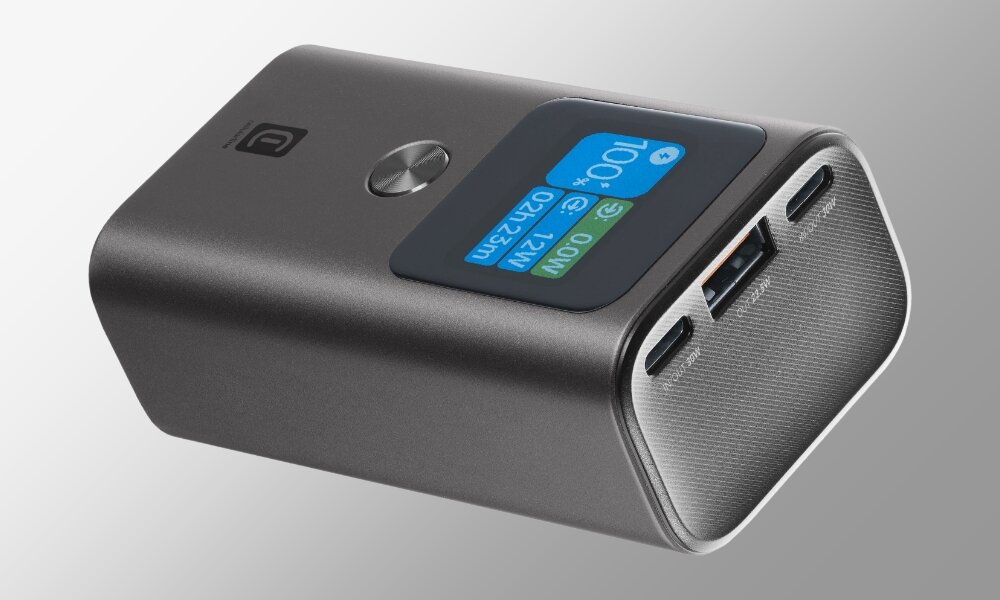 Antracytowy powerbank z wyświetlaczem pokazującym stan naładowania 100% oraz portami USB i USB-C. Na obudowie widoczne jest logo producenta.