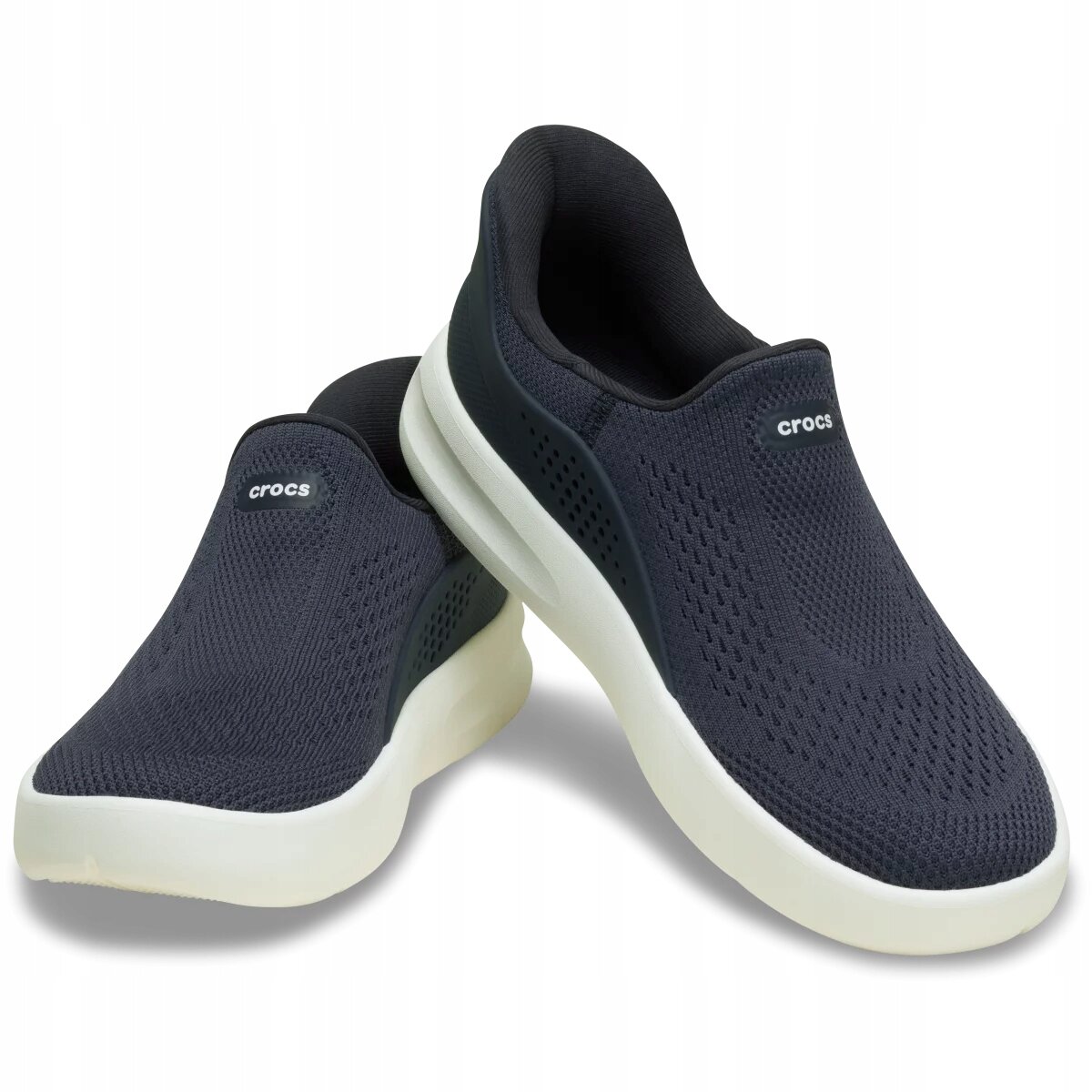 Na obrazie widoczne są ciemne buty sportowe typu slip-on z białą podeszwą. Na jednym z butów znajduje się napis \'crocs\'.