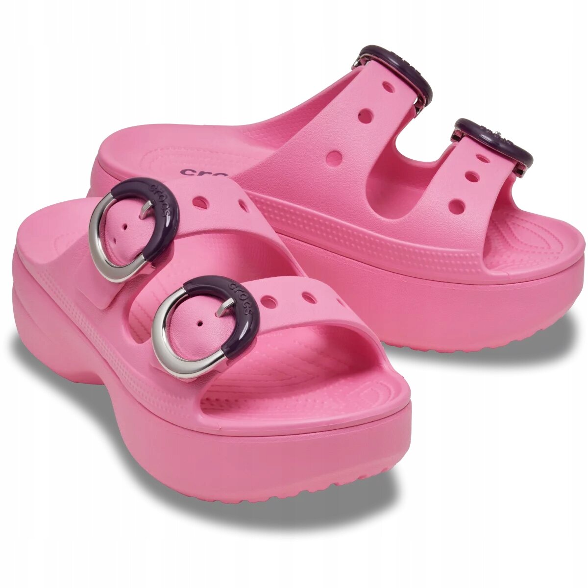 Różowe klapki na platformie z okrągłymi, ciemnymi klamrami i perforacjami na paskach. Na jednym z pasków widoczny jest napis \'crocs\'.