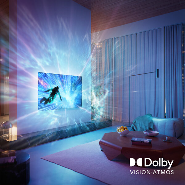 W salonie znajduje się telewizor wyświetlający dynamiczną scenę z efektem świetlnym rozprzestrzeniającym się na ścianę. W prawym dolnym rogu widoczne jest logo \'Dolby Vision Atmos\'.