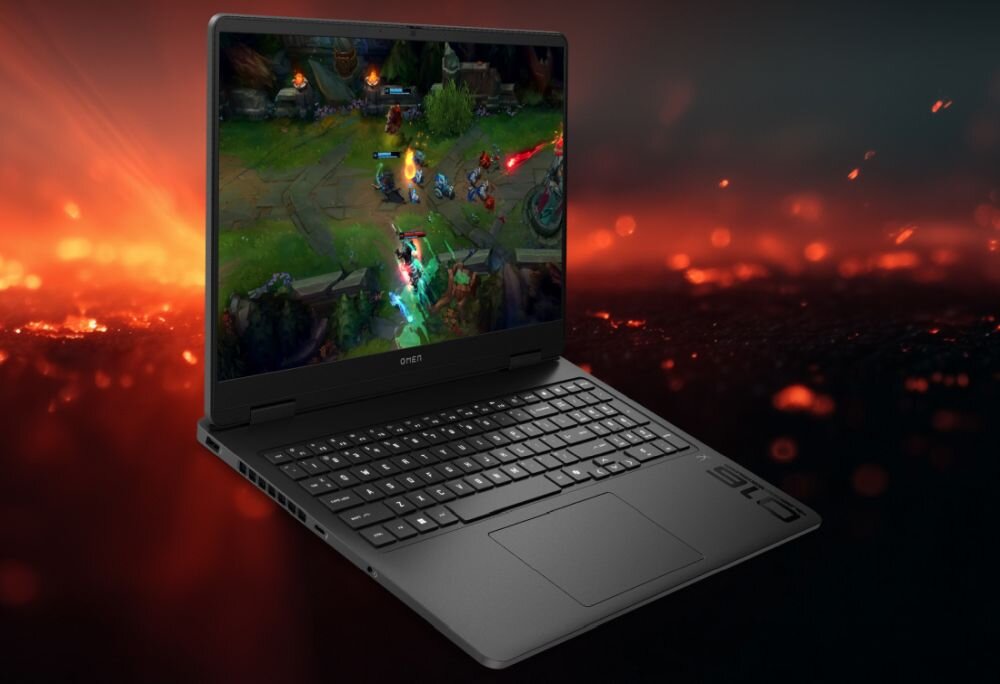 Laptop z wyświetlaczem pokazującym grę komputerową, na tle ognistego motywu. Na obudowie widoczne jest logo \'OMEN\'.