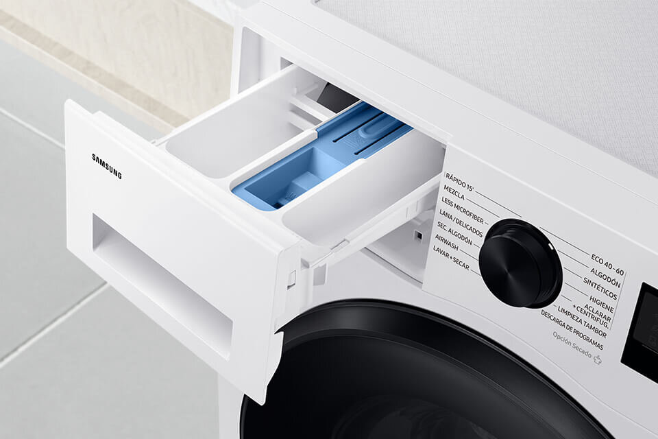 Obraz przedstawia otwarty dozownik na detergenty w pralce z widocznym logo \'SAMSUNG\'. Obok znajduje się panel z pokrętłem i napisami: \'RÁPIDO 15, MEZCLA, LAVAR MICROFIBER, LANA, DELICADOS, LAVAR ALGODÓN, AIRWASH, LAVAR+SECAR, ECO 40-60, ALGODÓN, SINTÉTICOS, HIGIENE, +ACLARADO, LIMPIEZA TAMBOR, DESCARGA ENERGÍA\'.