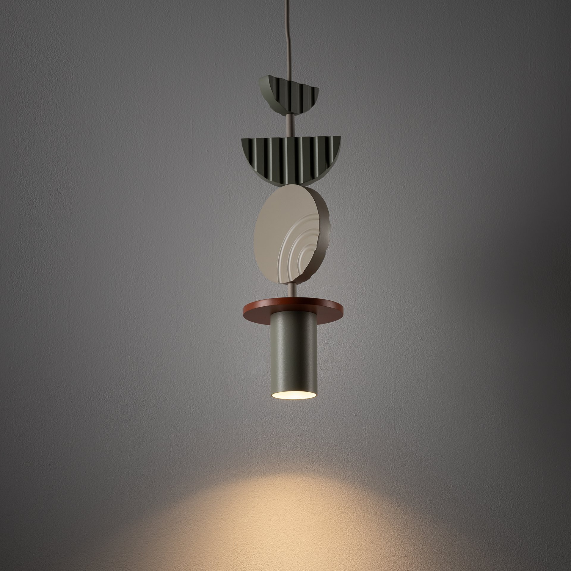 Lampa wisząca o nowoczesnym designie złożona z kilku geometrycznych elementów w różnych kolorach, emitująca światło skierowane w dół. Ściana w tle jest gładka i jednolita.