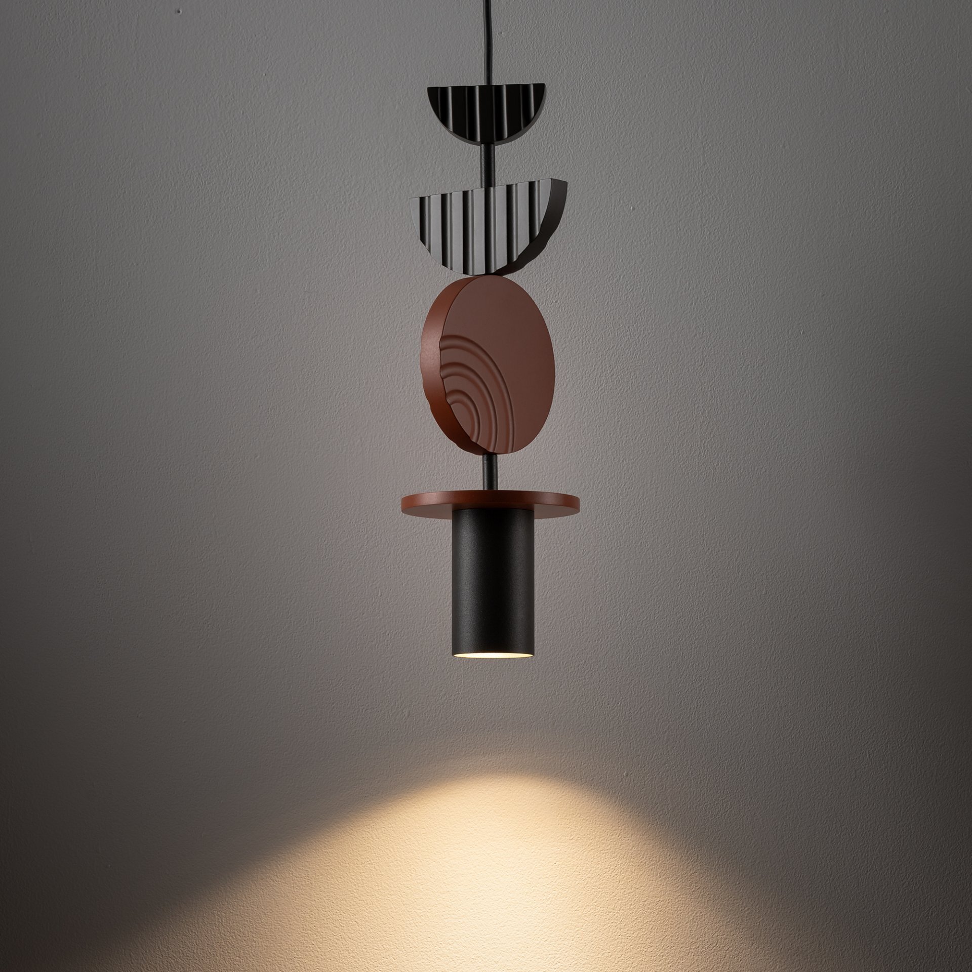 Lampa wisząca o nowoczesnym designie z elementami geometrycznymi w kolorach czarnym i brązowym, emitująca światło skierowane w dół. Światło tworzy jasną plamę na ścianie.