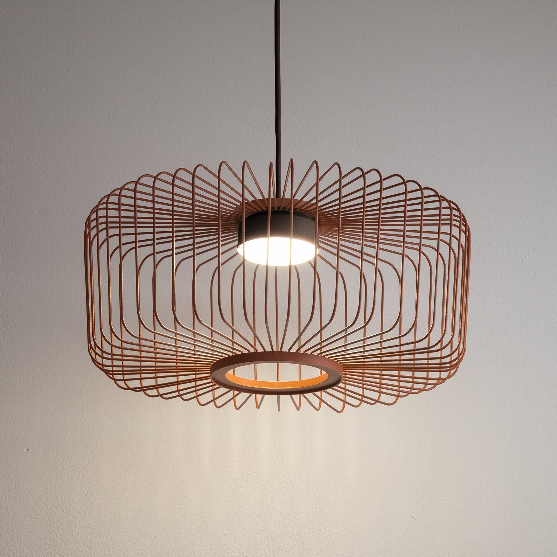 Lampa wisząca z metalowym kloszem w kształcie siatki, emitująca światło z centralnego punktu. Klosz ma kolor miedziany i jest zawieszony na czarnym przewodzie.