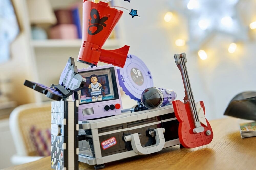 Zestaw LEGO przedstawiający kolorową skrytkę z elementami muzycznymi, w tym czerwoną gitarą i megafonem z czarnym wzorem. Na skrytce widoczny jest napis \'MAGIC\' oraz postać w okienku.