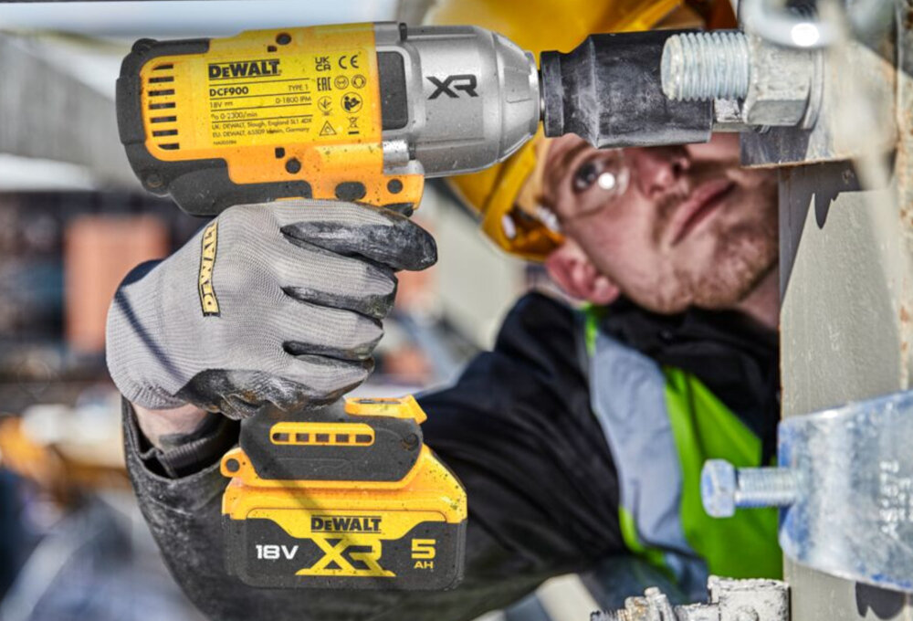 Osoba używa żółto-czarnego klucza udarowego DEWALT DCF900P2T do dokręcania śruby. Na urządzeniu widoczne są napisy: \'DEWALT\', \'DCF900\', \'XR\', \'18V\', \'5 AH\'.