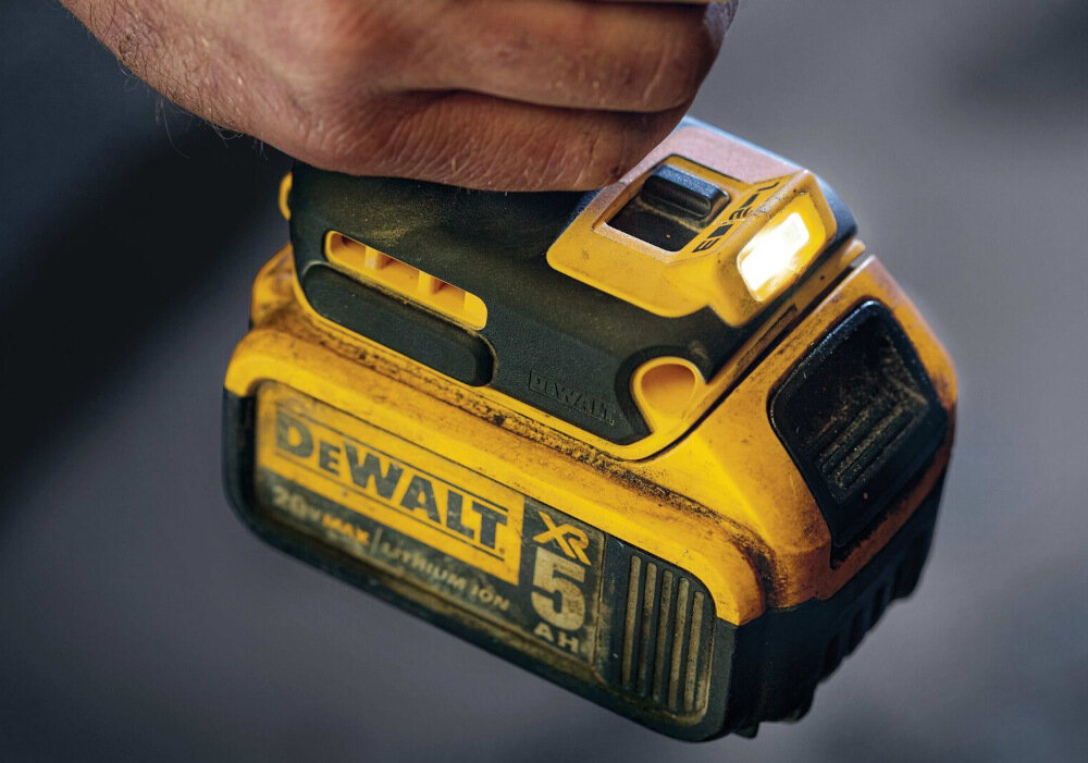 Osoba trzyma żółto-czarny klucz udarowy z widocznym logo \'DEWALT XR 5 AH\'. Urządzenie ma podświetlenie LED i jest w użyciu.