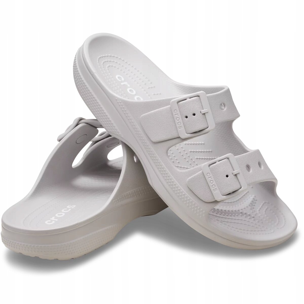 Na obrazie widoczne są białe klapki z dwoma paskami z klamrami, na których znajduje się napis \'crocs\'. Klapki mają perforowaną powierzchnię wewnętrzną i logo \'crocs\' na podeszwie.