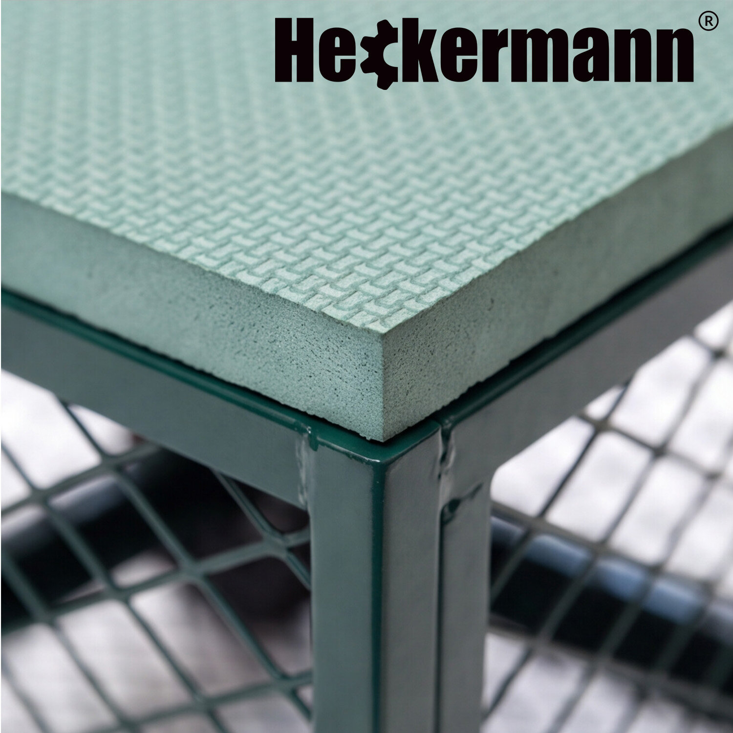 Zbliżenie na narożnik zielonego wózka ogrodowego z metalową siatką i teksturowaną powierzchnią. Widoczne logo \'Heckermann\'.